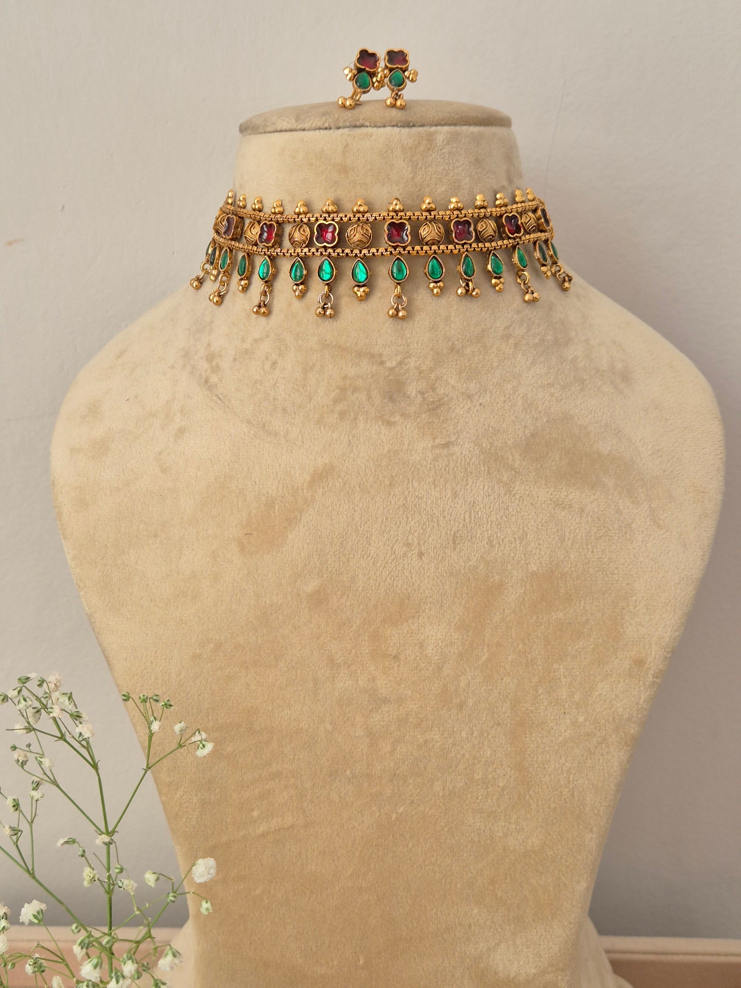A gold-plated choker necklace featuring a row of square red gemstones and hanging green teardrop beads by naitri.in