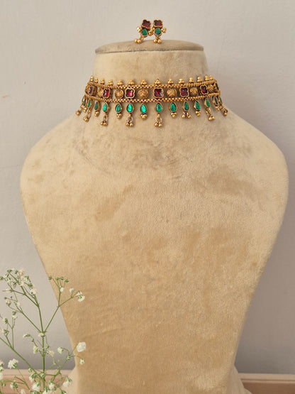 A gold-plated choker necklace featuring a row of square red gemstones and hanging green teardrop beads by naitri.in