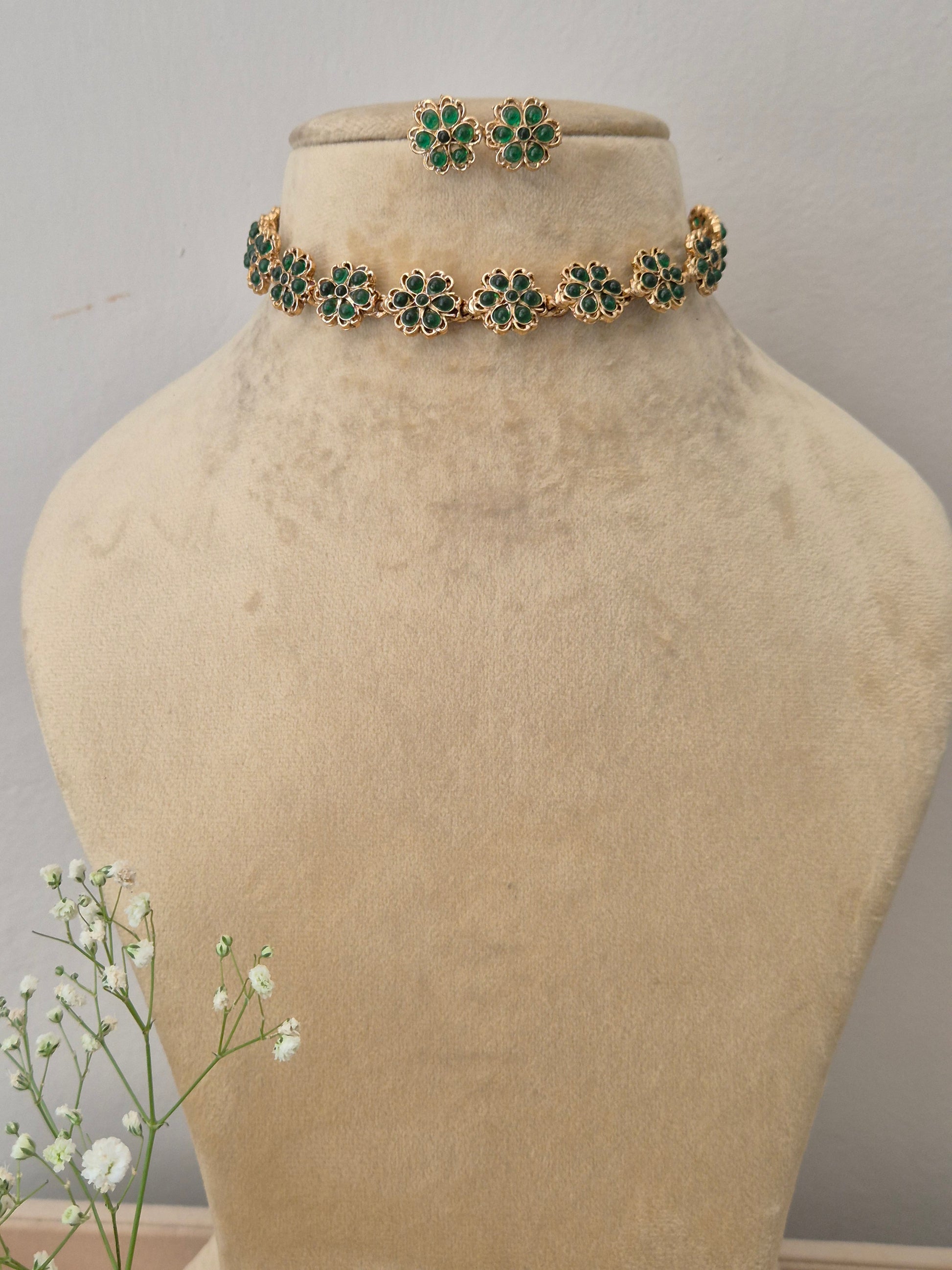 A gold-plated choker necklace featuring intricate green gemstone floral motifs, with matching flower stud earrings by naitri.in