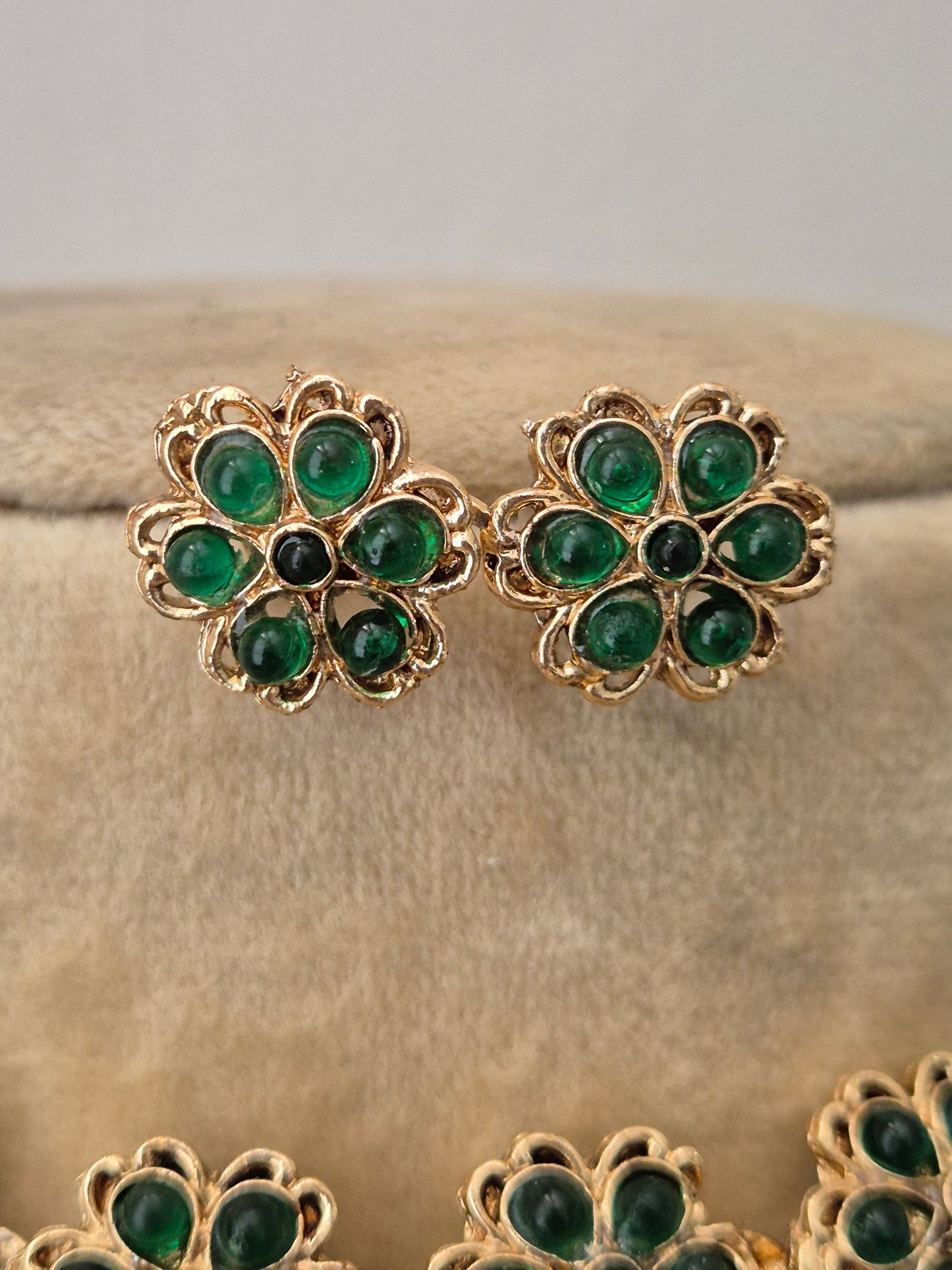 Gold earrings embedded with vibrant green stones in a repeating floral pattern by naitri.in
