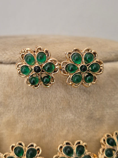 Gold earrings embedded with vibrant green stones in a repeating floral pattern by naitri.in