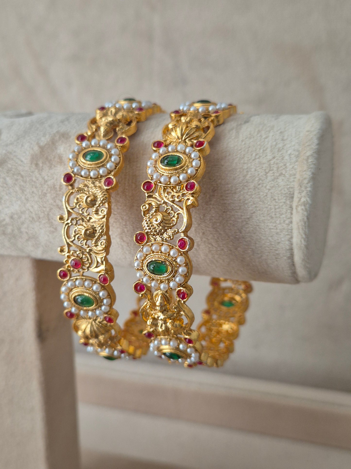 Set of two traditional gold-toned festive bangles with red and green stones by naitri.in