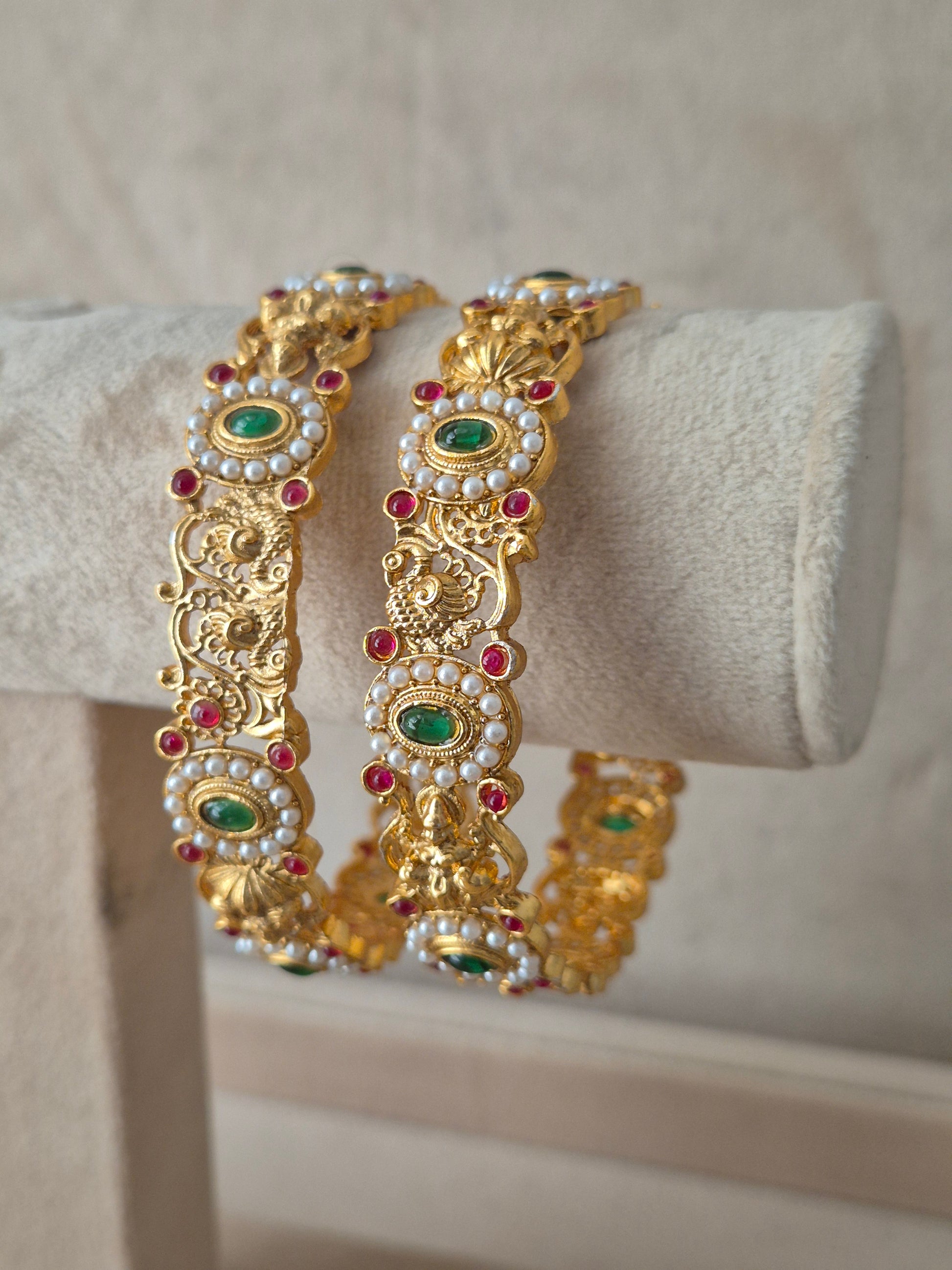 Set of two traditional gold-toned festive bangles with red and green stones by naitri.in