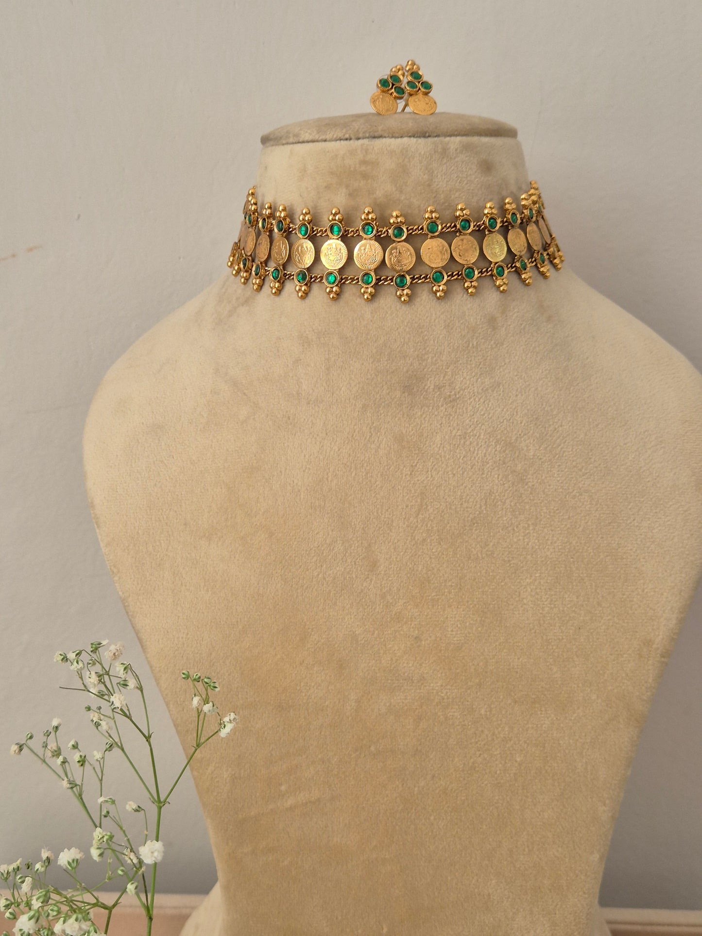 A gold-plated traditional ethnic choker necklace featuring a row of circular coin motifs and hanging green bead droplets, with matching earrings by naitri.in