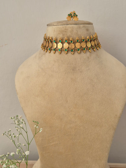 A gold-plated traditional ethnic choker necklace featuring a row of circular coin motifs and hanging green bead droplets, with matching earrings by naitri.in