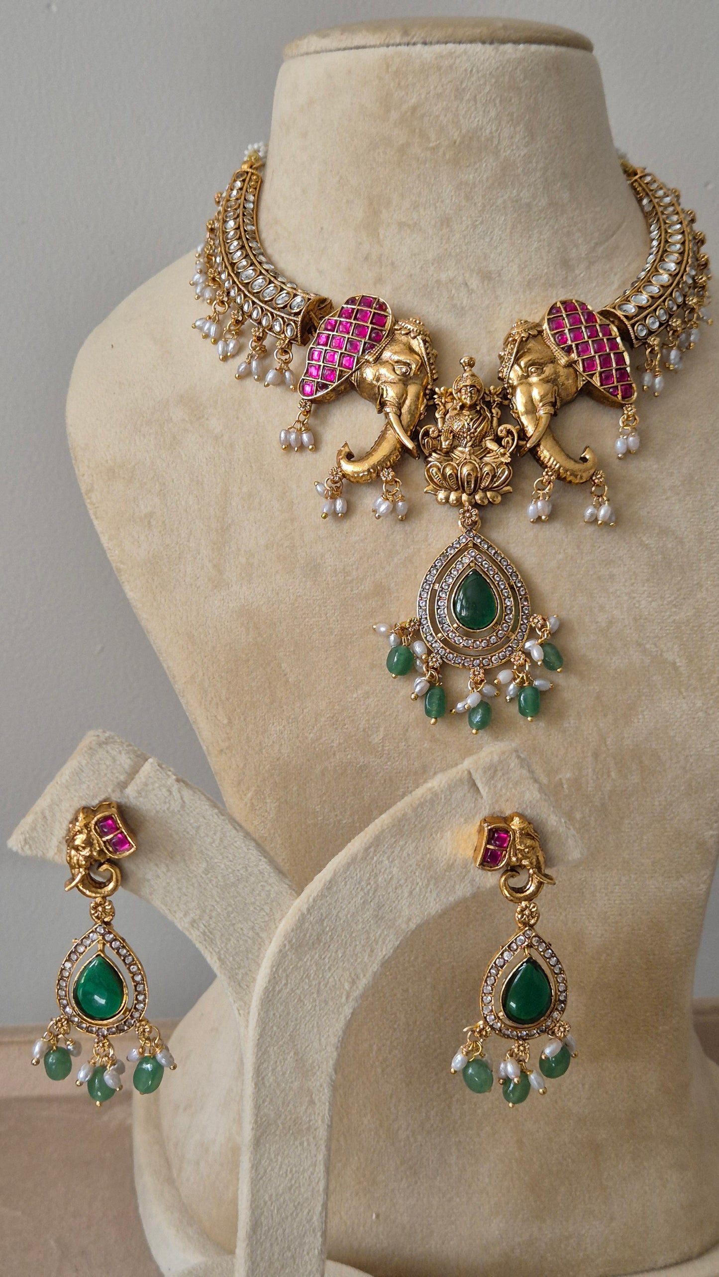 Handcrafted antique gold jewelry with intricate craftsmanship, featuring vibrant gemstones and traditional ethnic design Gold temple necklace set with pink elephant motifs, green beads, and Lakshmi pendant with matching drop earrings by naitri.in