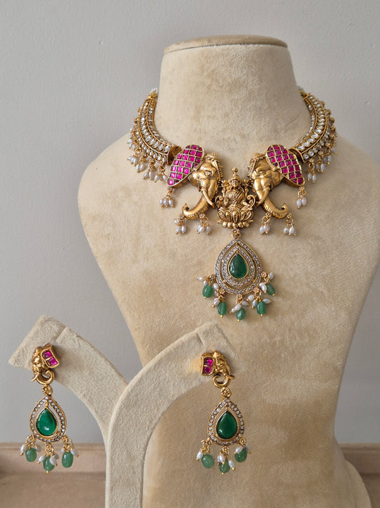 Ornate gold-plated temple necklace set with pink stone-studded elephant motifs, a Goddess Lakshmi pendant, and green bead droplets with matching earrings by naitri.in