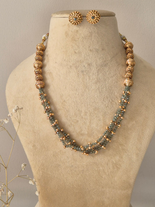 Handcrafted  set featuring three strands of small grey and gold beads, accented with larger textured gold beads and matching circular stud earrings by naitri.in