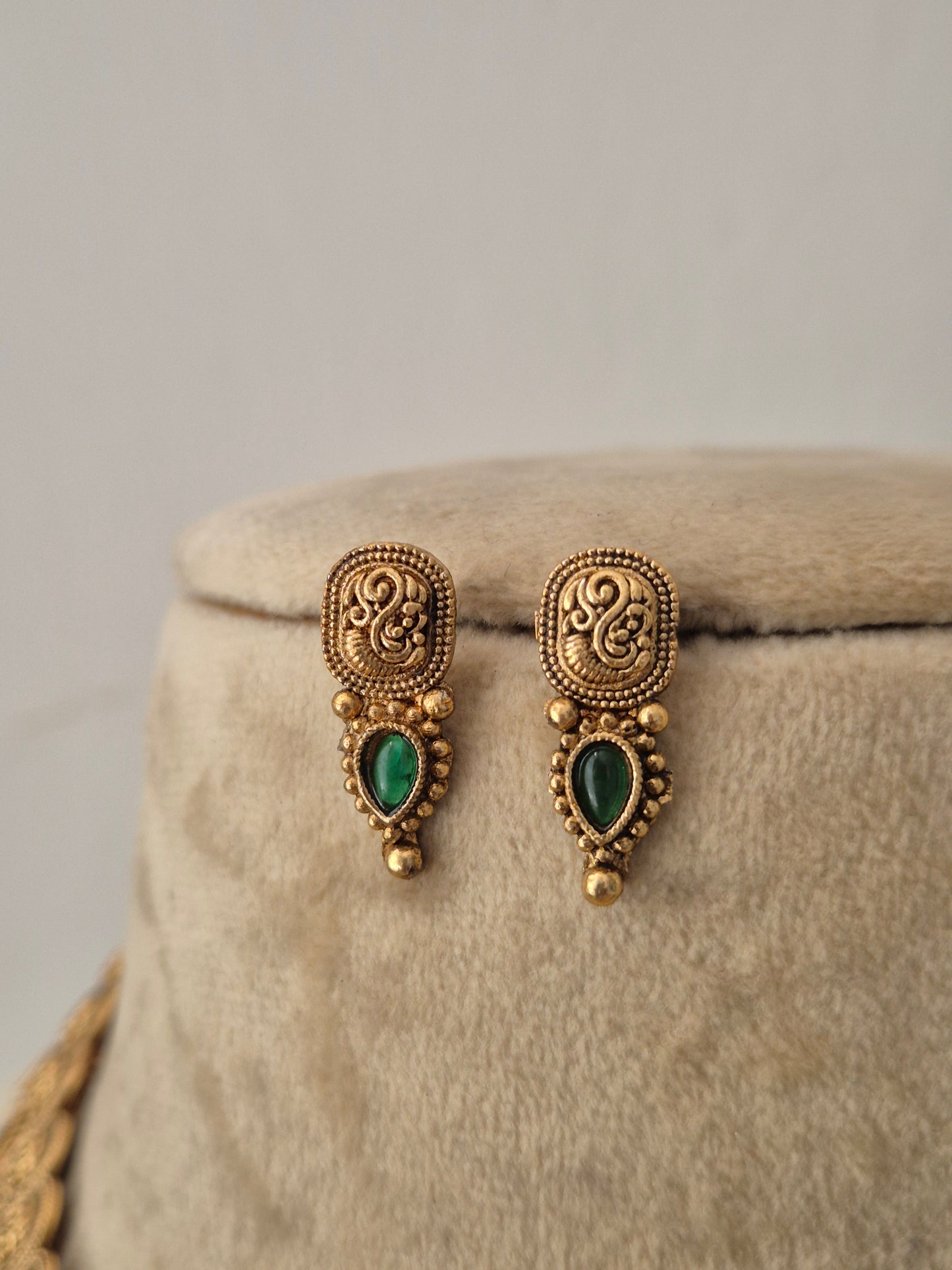 A pair of gold-toned traditional earrings with green teardrop-shaped stones, by naitri.in