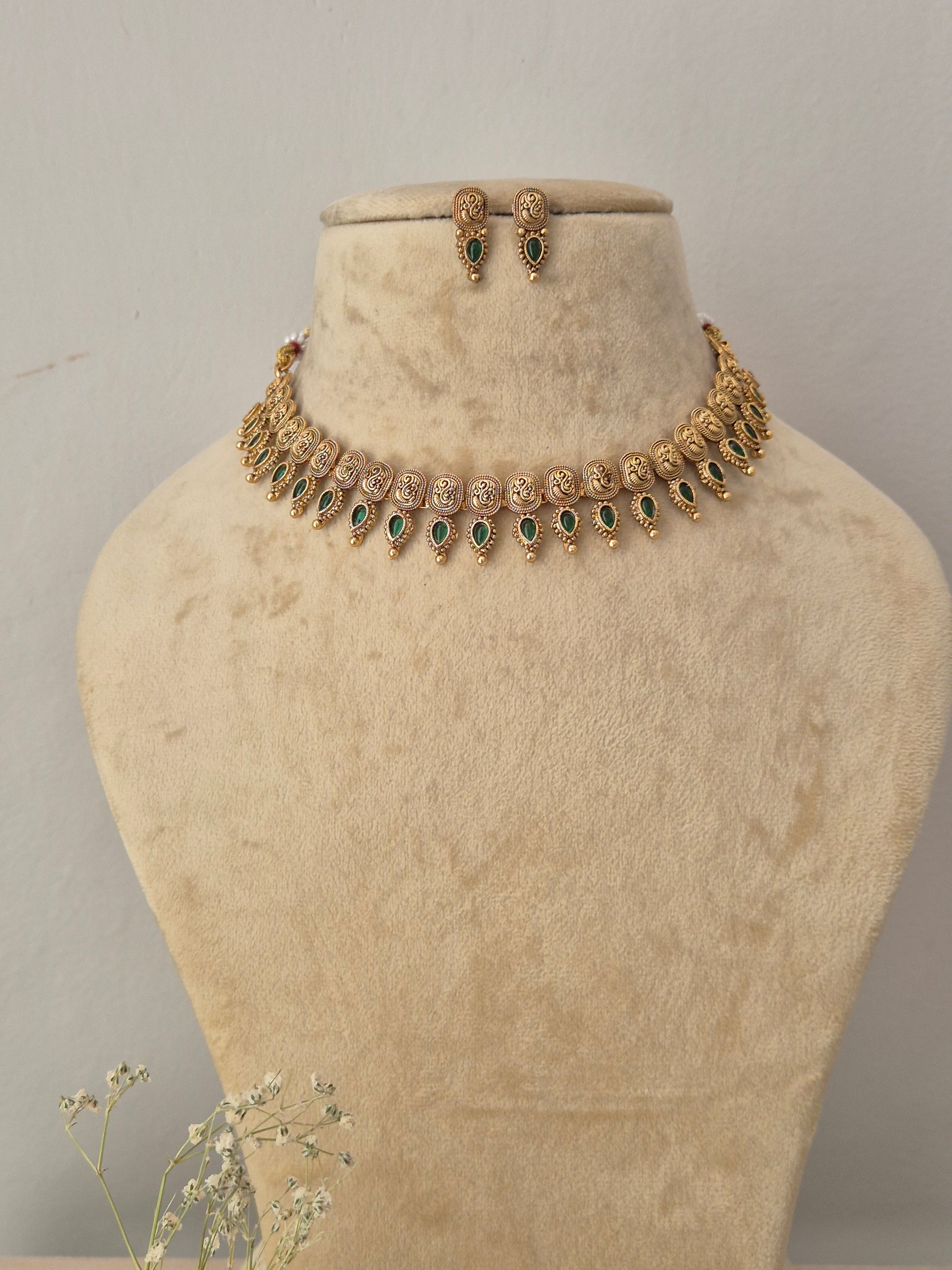 Gold-toned traditional Indian choker necklace and matching small dangle earrings set the necklace features intricate metalwork patterns with a lower fringe of delicate hanging green gemstone drops, by naitri.in