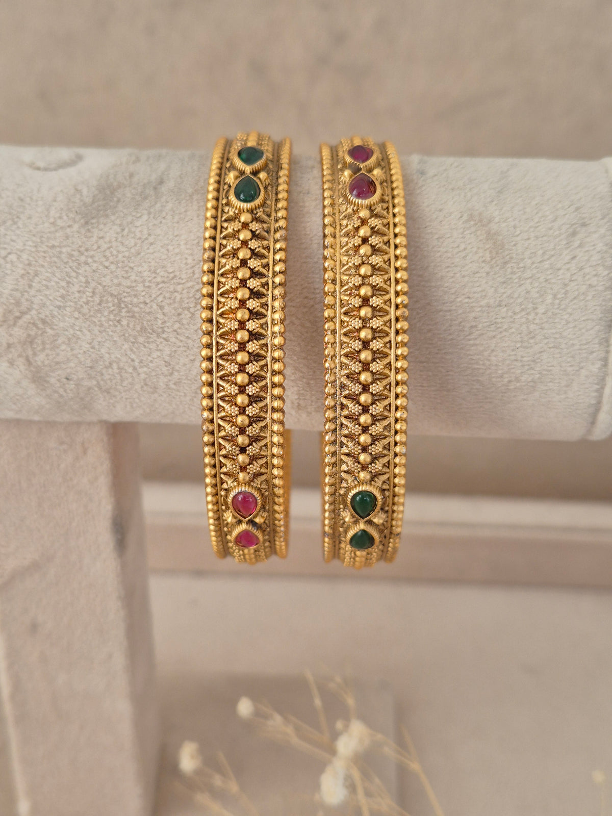 Set of two textured gold-plated bangles with red and green gemstone accents by naitri.in
