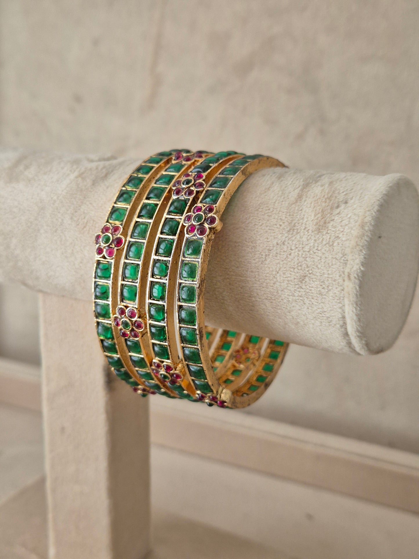 A stack of four gold bangles adorned with green square stones and pink floral accents, Traditional Indian festive bangles adorned with green gemstones and pink floral stone clusters by naitri.in