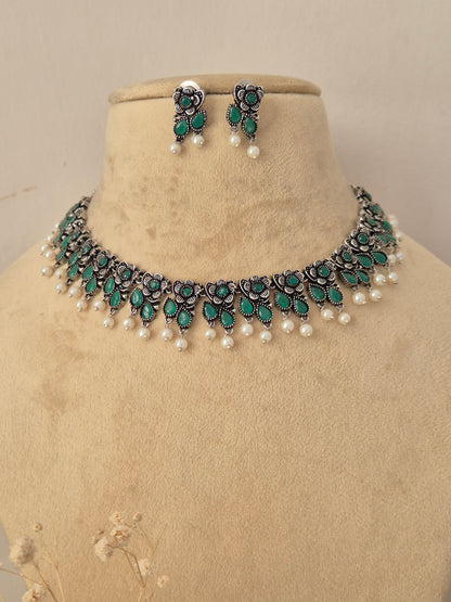 Pair of oxidized silver floral motif choker necklace with matching green stone earrings by Naitri.in