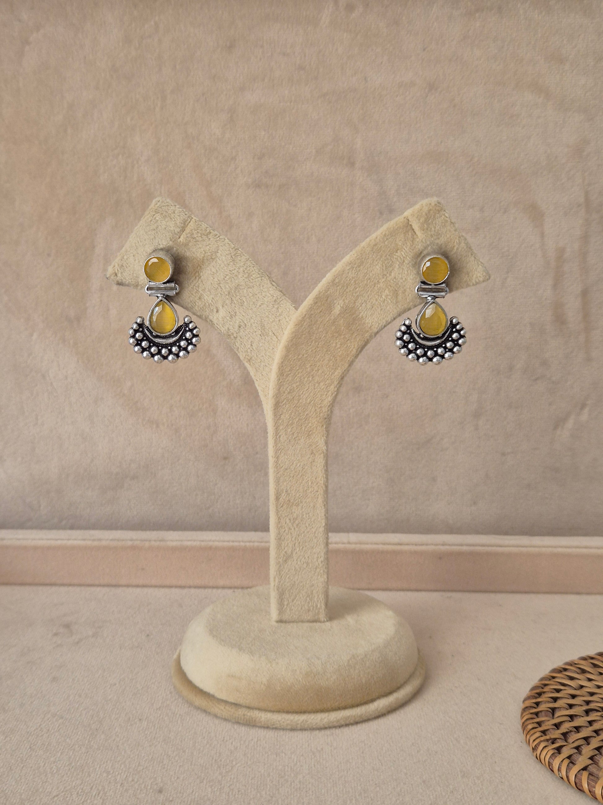 Pair of Grishma silver-toned dangle earrings featuring translucent yellow stone drops and a textured crescent accent by naitri.in