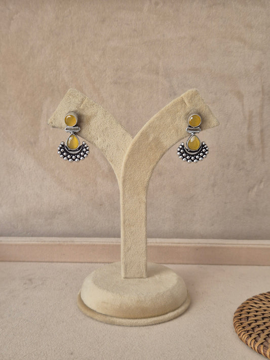 Pair of Grishma silver-toned dangle earrings featuring translucent yellow stone drops and a textured crescent accent by naitri.in