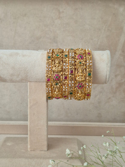 Traditional brass alloy gold-tone bangles set of 6 adorned with carved temple motifs and ruby red and emerald green stone inlay by naitri.in