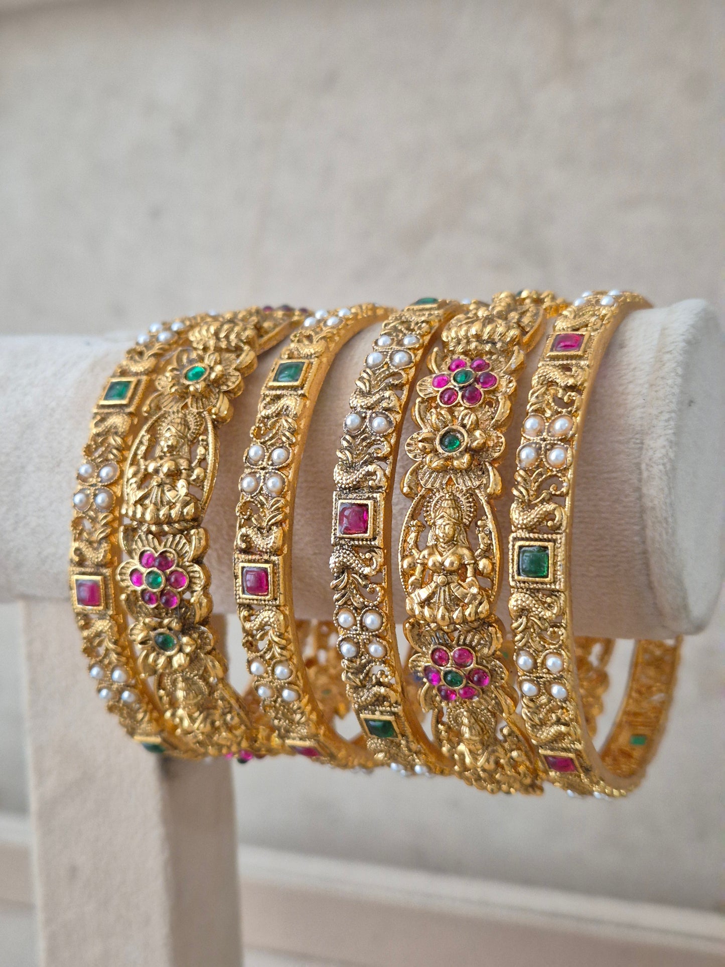 Festive antique gold bangle stack featuring traditional goddess carved patterns and colorful stone accents by naiti.in