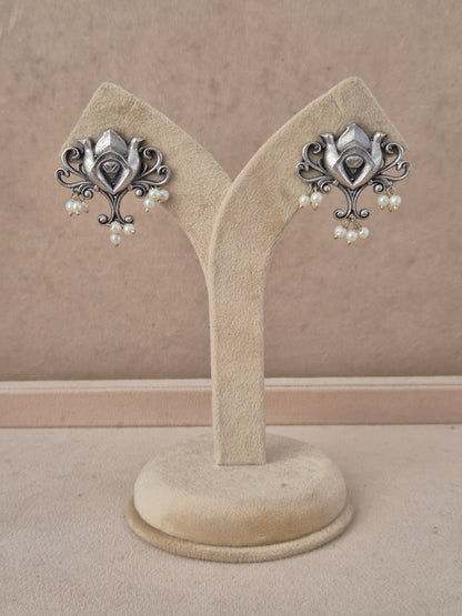 A pair of ornate silver-toned earrings with small white pearl drops, by naitri.in