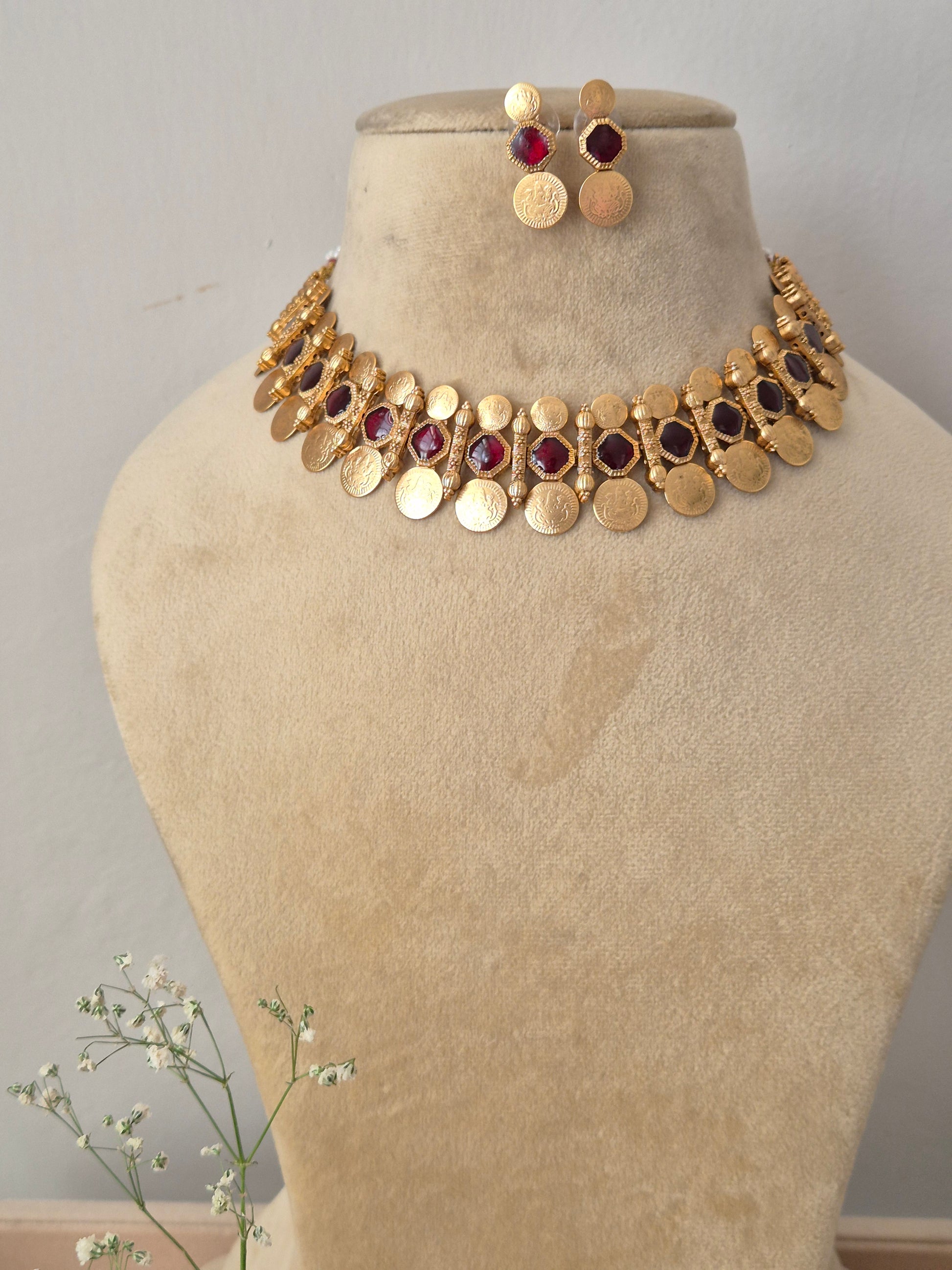 Handcrafted gold-polished brass choker necklace featuring alternating red stone accents and dangling round coin charms, with matching round gold stud earrings by naitri.in