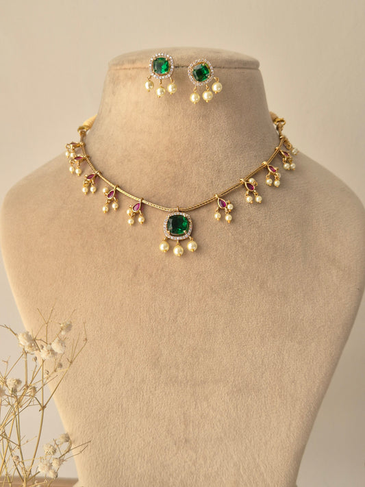 Gold-plated Hamsa necklace set featuring emerald green square-cut gemstones, ruby red accents, and delicate pearl drops by naitri.in