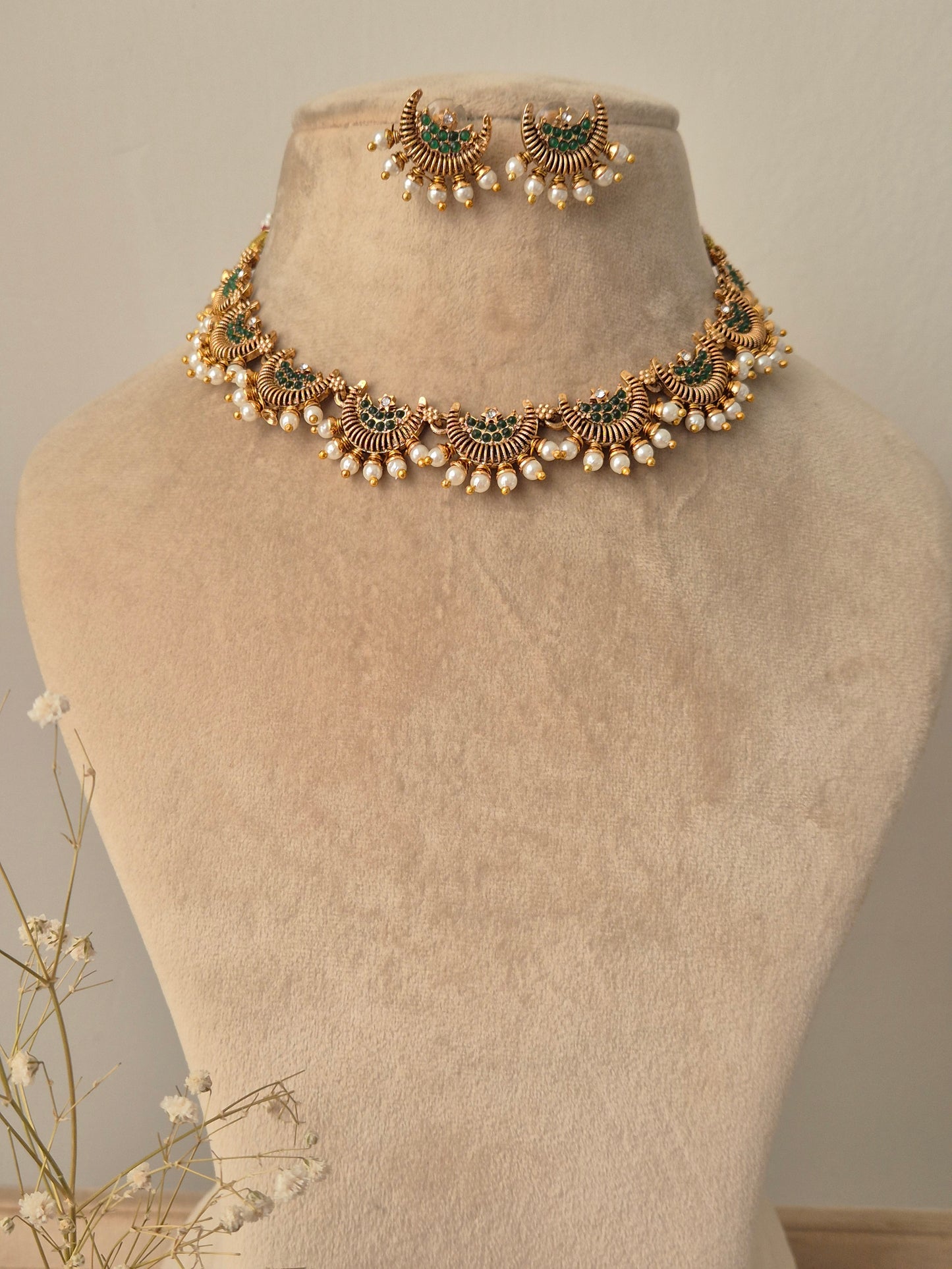 Gold jewelry design half-moon with small green stones in middle and pearls attached outside and same design earrings by naitri.in