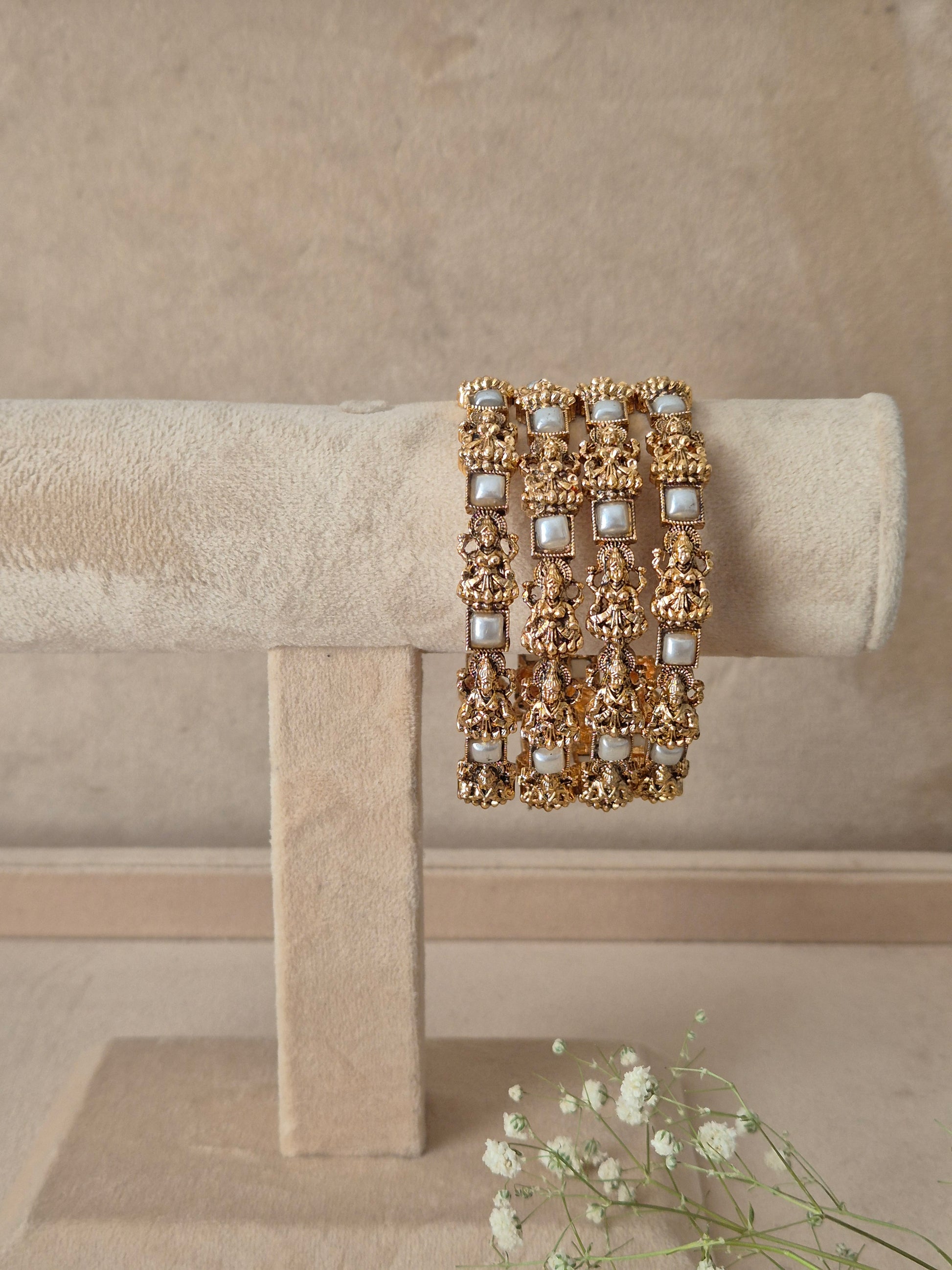Set of 4 antique gold-plated bangles featuring detailed temple-style carved motifs interspersed with square pearl/white gemstone accents by naitri.in