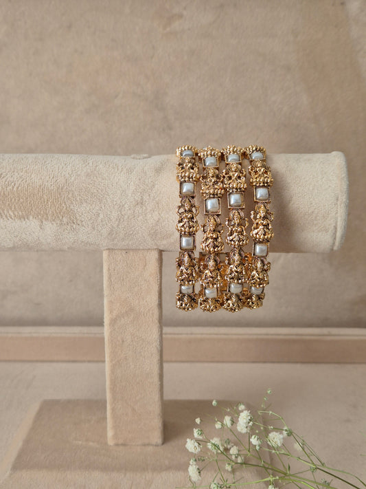 Set of 4 antique gold-plated bangles featuring detailed temple-style carved motifs interspersed with square pearl/white gemstone accents by naitri.in