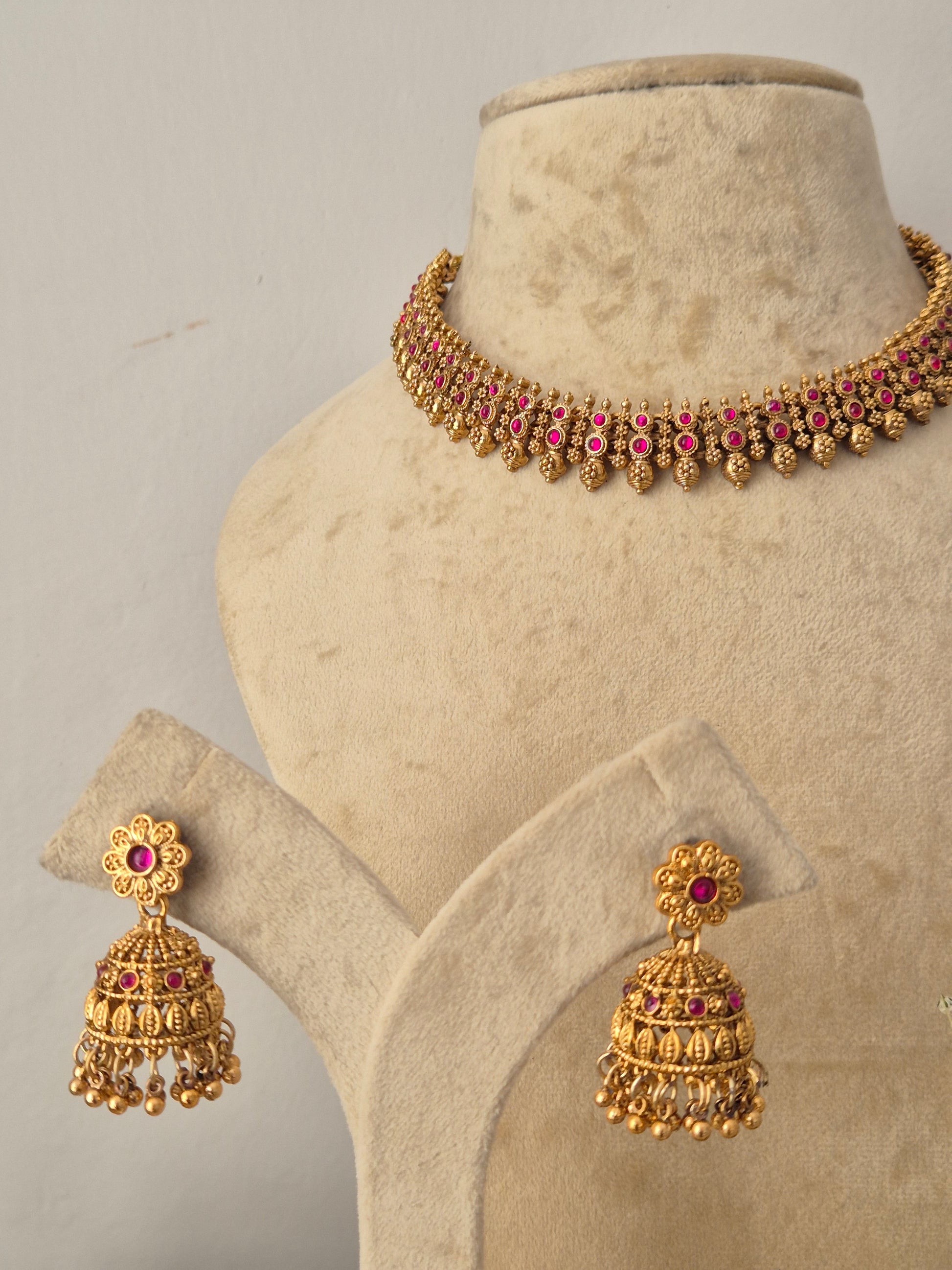 Traditional Indian gold-toned choker necklace and matching jhumka earrings embellished with deep pink gemstone accents, by naitri.in