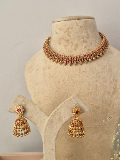 Gold-toned traditional Indian jewelry set featuring a choker necklace and matching jhumka earrings, embellished with gold-plated filigree and small pink gemstone accents, by naitri.in
