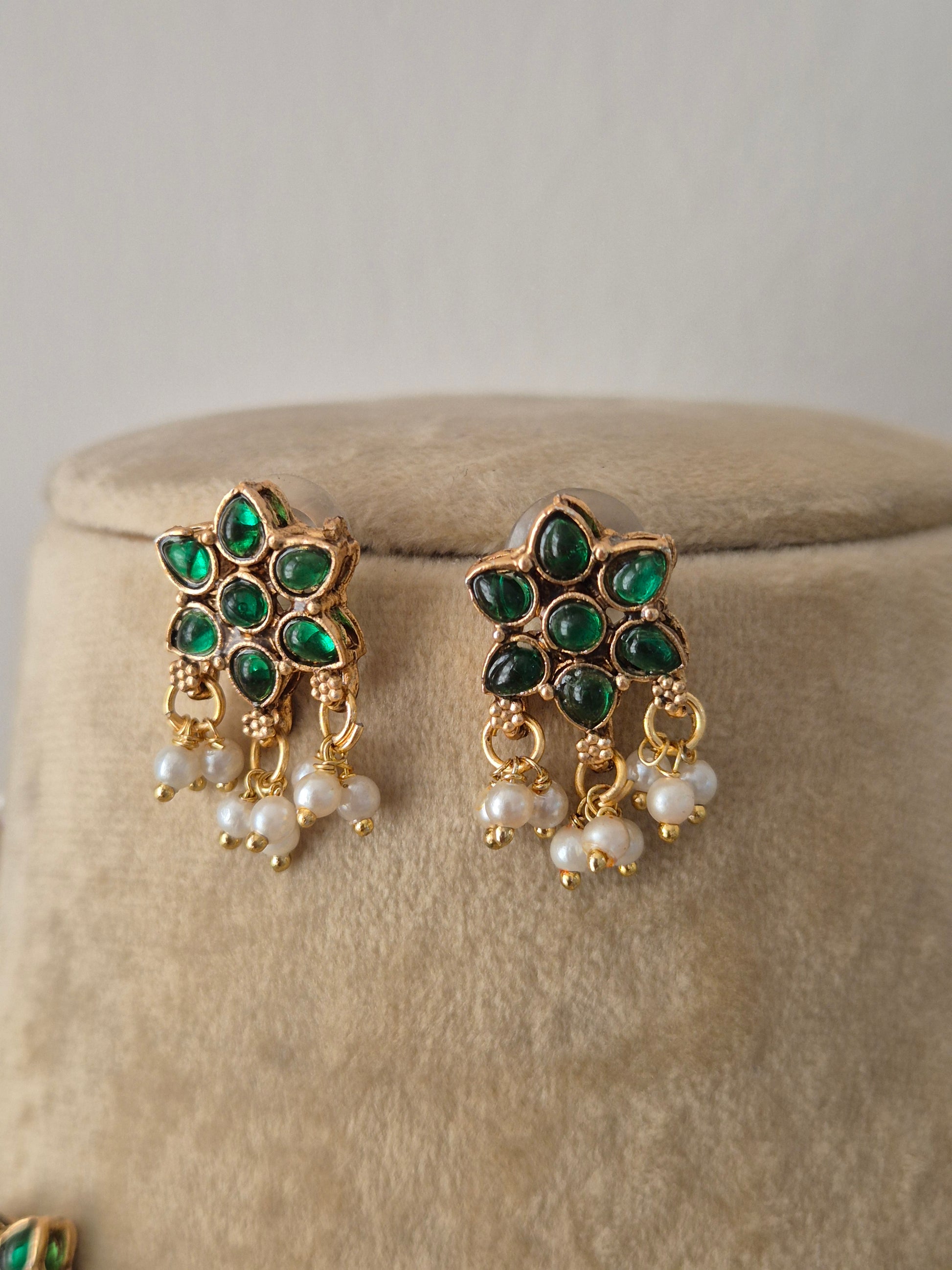 Pair of gold earrings embedded with green gemstones and white pearl drops, by naitri.in