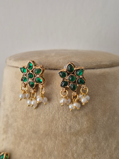 Pair of gold earrings embedded with green gemstones and white pearl drops, by naitri.in