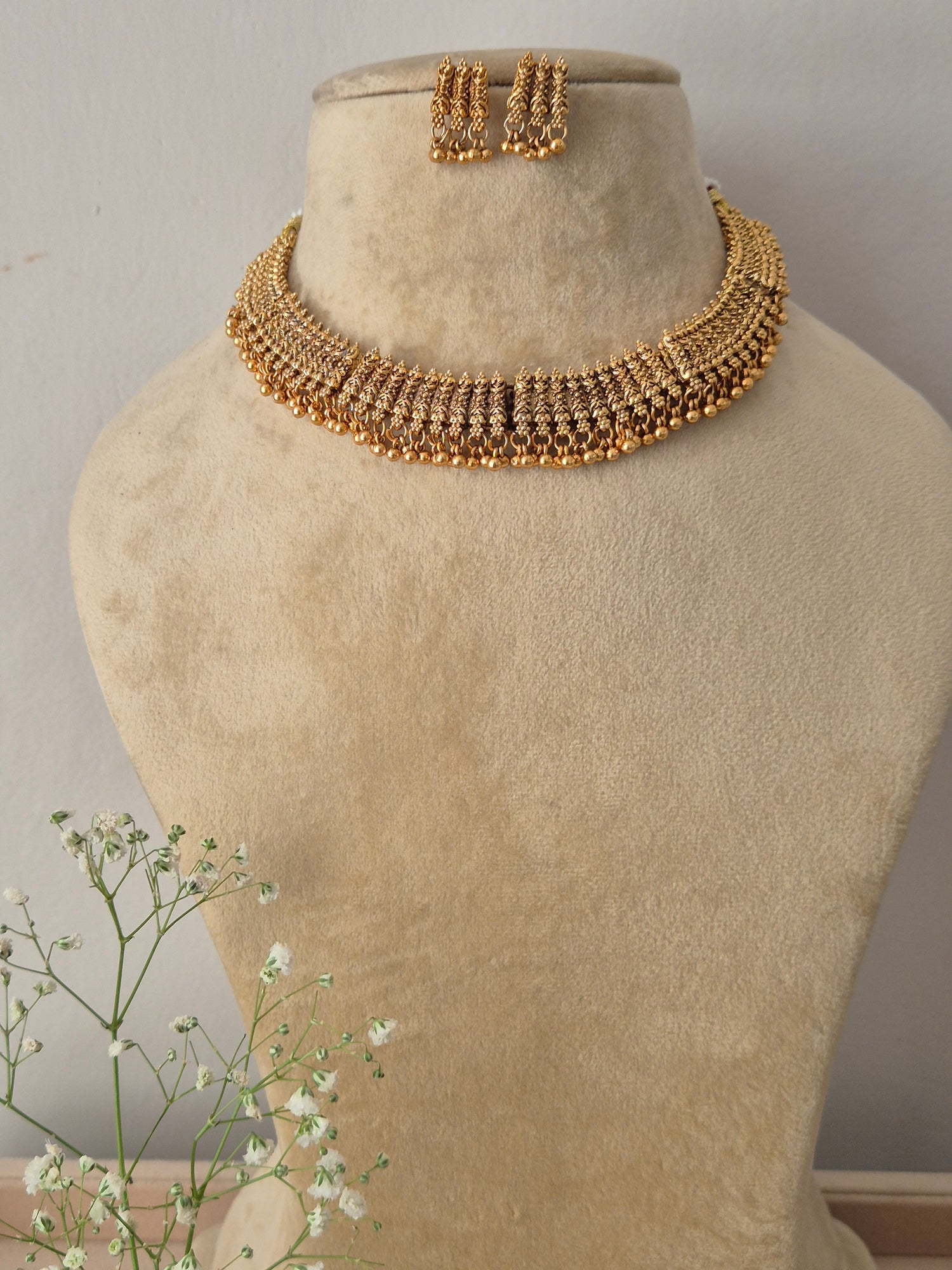 A gold-plated choker necklace featuring a wide band of intricate, textured gold patterns and a row of hanging golden bead droplets, by naitri.in 