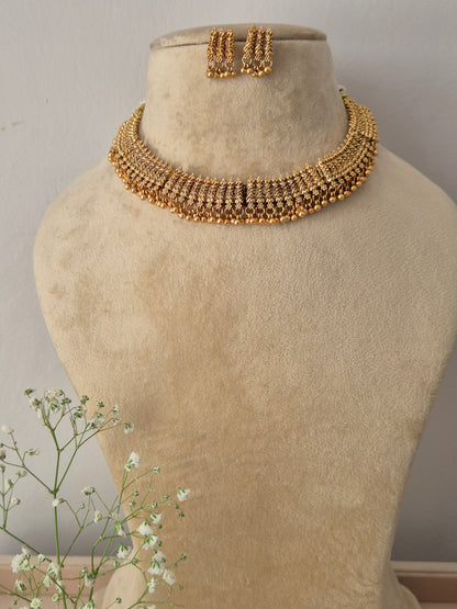 A gold-plated choker necklace featuring a wide band of intricate, textured gold patterns and a row of hanging golden bead droplets, by naitri.in 