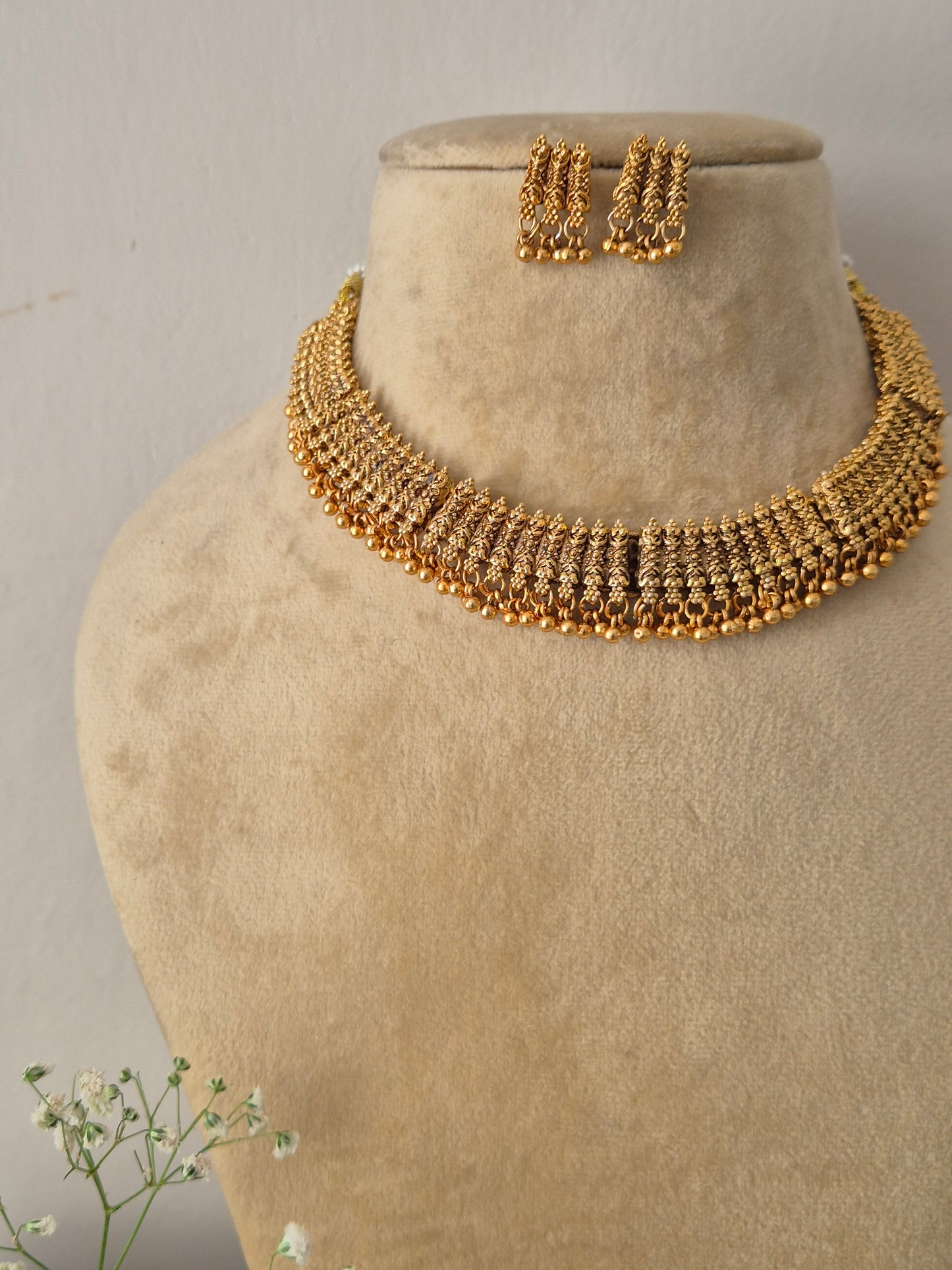 Elegant gold-toned traditional choker jewelry set featuring intricate metalwork, gold-plated Harsha necklace and earring set with antique gold finishes by naitri.in