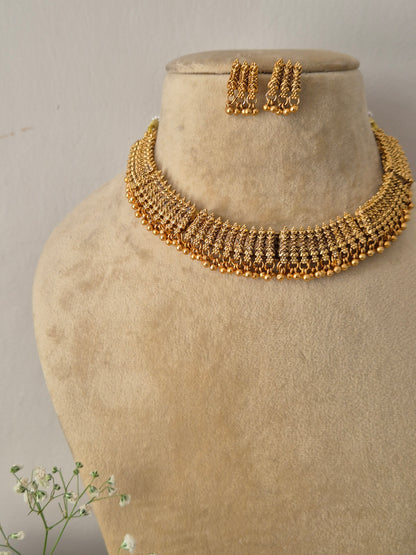 Elegant gold-toned traditional choker jewelry set featuring intricate metalwork, gold-plated Harsha necklace and earring set with antique gold finishes by naitri.in
