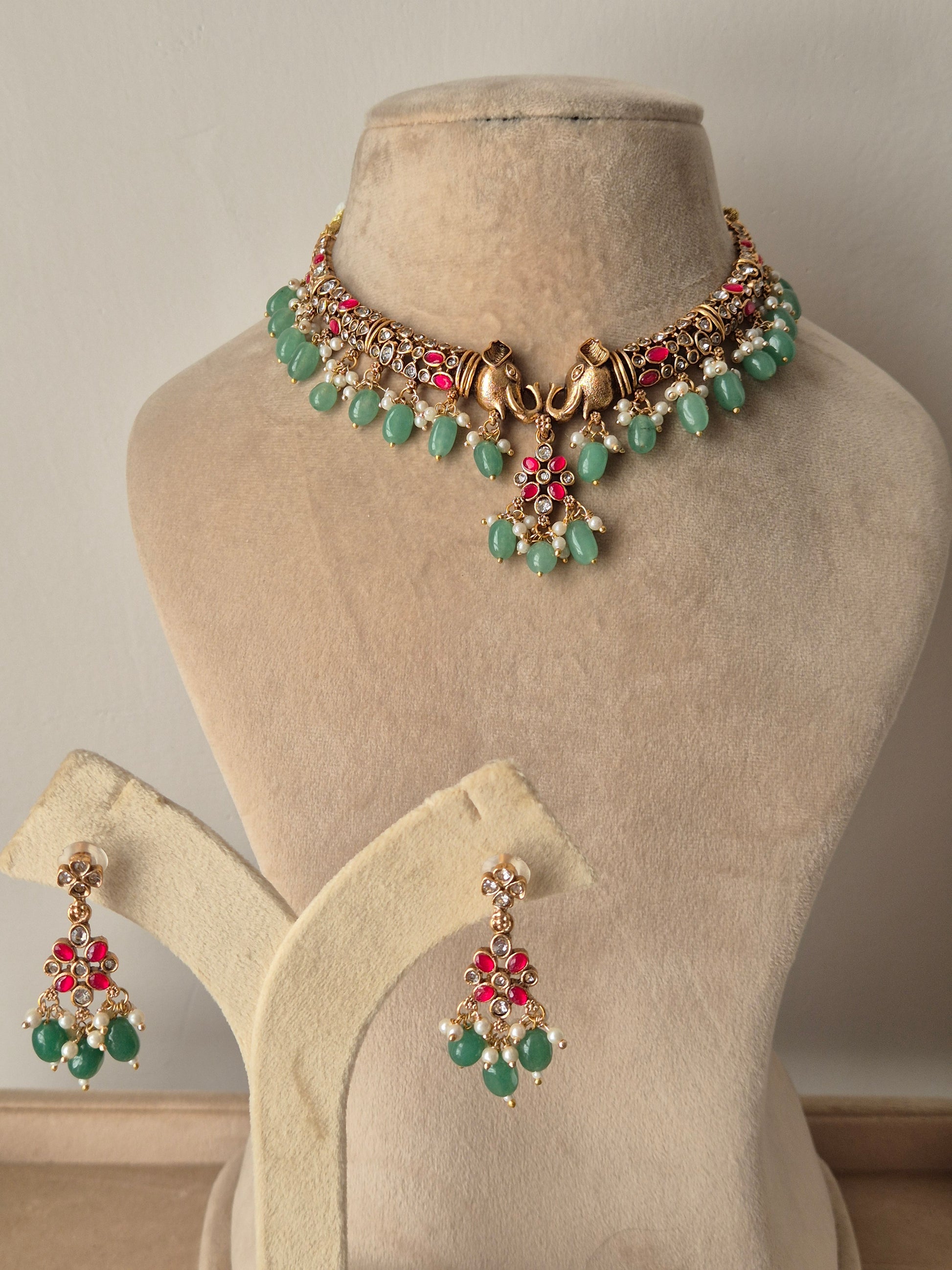 Close-up of the Hasmita Necklace Set, an artisanal brass alloy jewelry set with intricate gold-plated motifs, pink embellishments, and hanging green stones by naitri.in