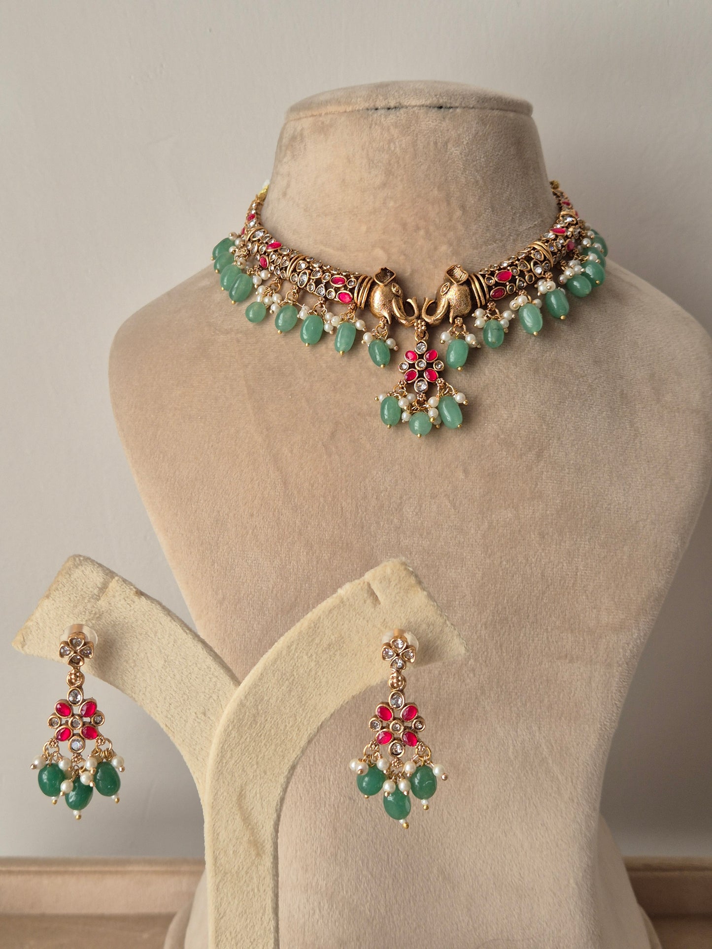  Necklace Set featuring a golden brass choker with pink stones, pearl detailing, and green bead droplets, displayed with matching dangle earrings by naitri.in