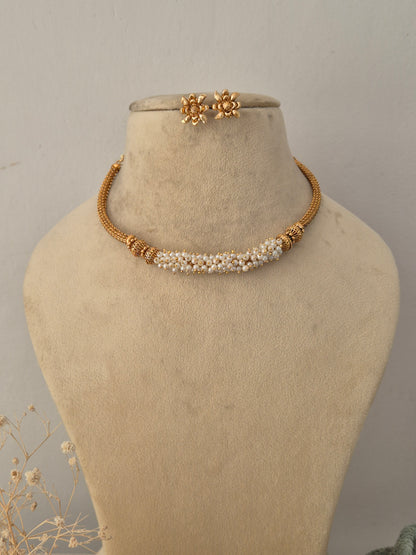 Heena gold-toned ethnic choker necklace set featuring a delicate cluster of pearls, textured gold beads, and matching floral stud earrings displayed on a beige mannequin by Naitri.in