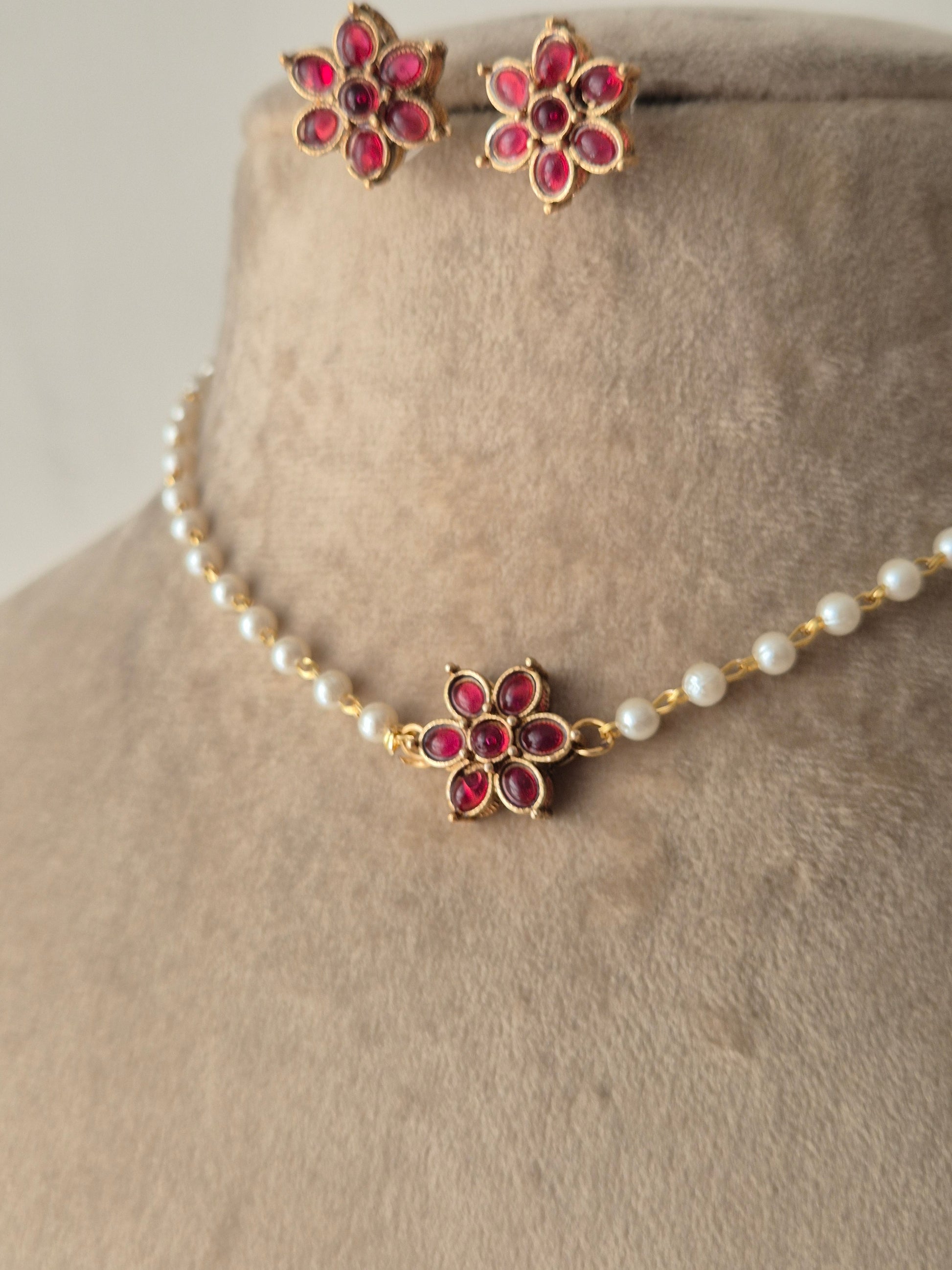 A delicate pearl strand choker featuring a central gold-plated floral motif with pink stones, shown with matching small floral stud earrings by naitri.in