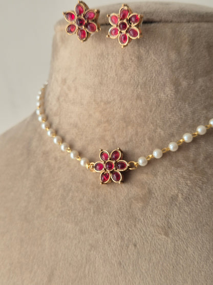 A delicate pearl strand choker featuring a central gold-plated floral motif with pink stones, shown with matching small floral stud earrings by naitri.in