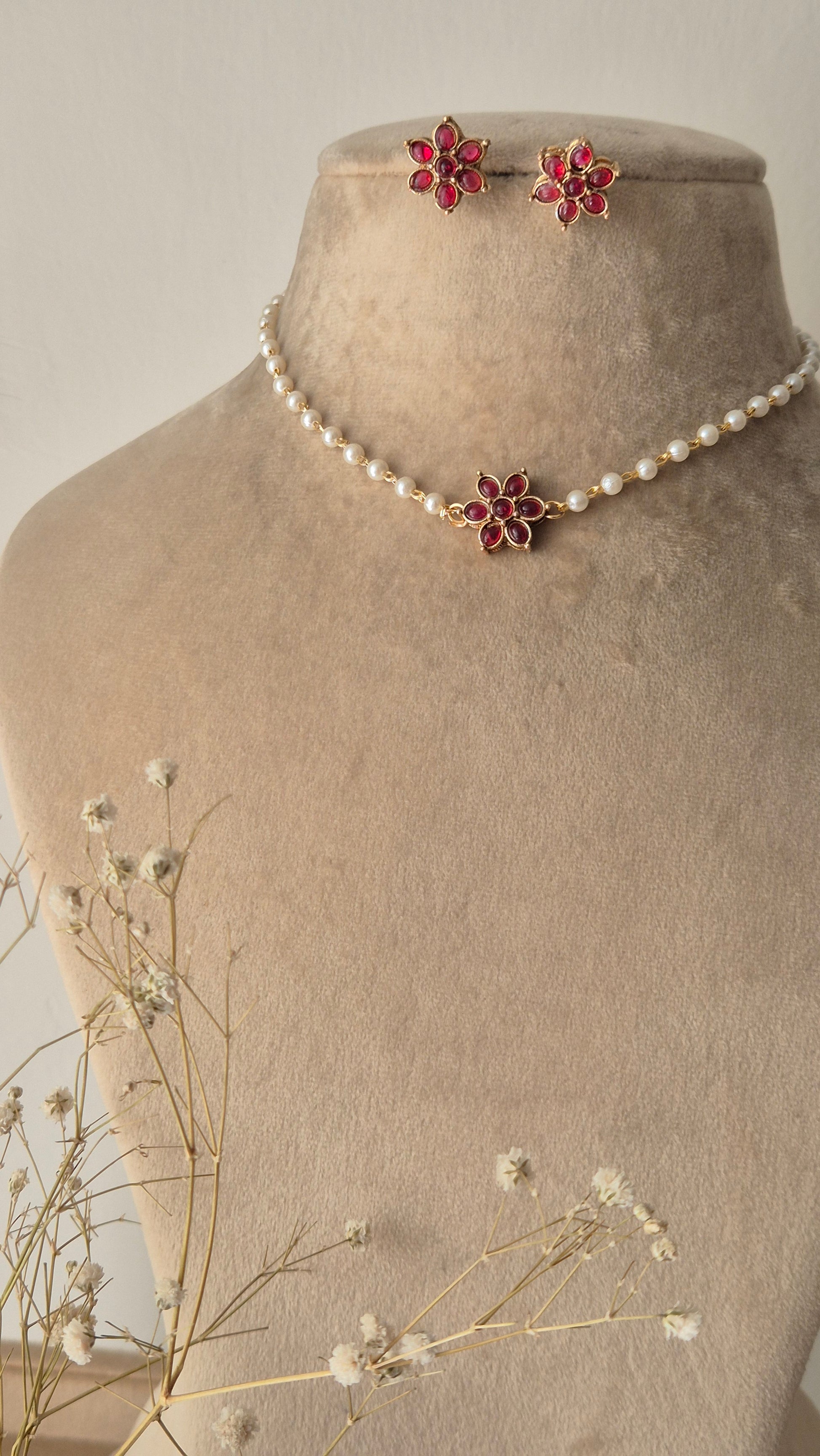 Pearl choker necklace with a pink stone floral pendant, A delicate pearl strand choker featuring a central gold-plated floral motif with pink stones by naitri.in