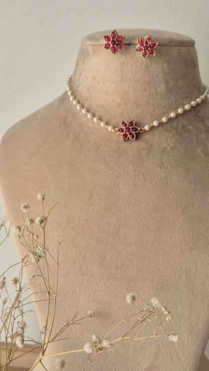 Pearl choker necklace with a pink stone floral pendant, A delicate pearl strand choker featuring a central gold-plated floral motif with pink stones by naitri.in