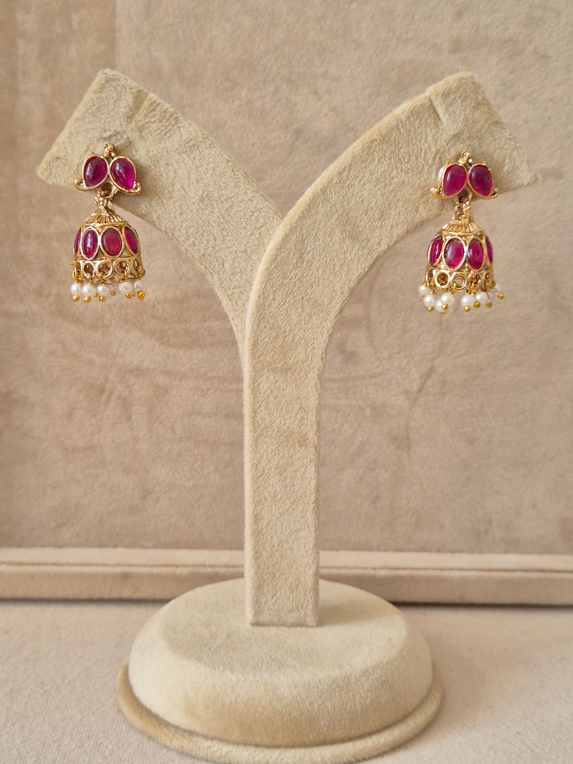Traditional gold-toned Heli Jhumka earrings featuring pink gemstone studs, intricate floral engravings on the bell, and white pearl-like bead clusters by naitri.in