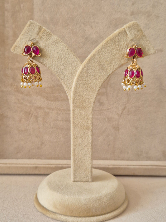 Traditional gold-toned Heli Jhumka earrings featuring pink gemstone studs, intricate floral engravings on the bell, and white pearl-like bead clusters by naitri.in