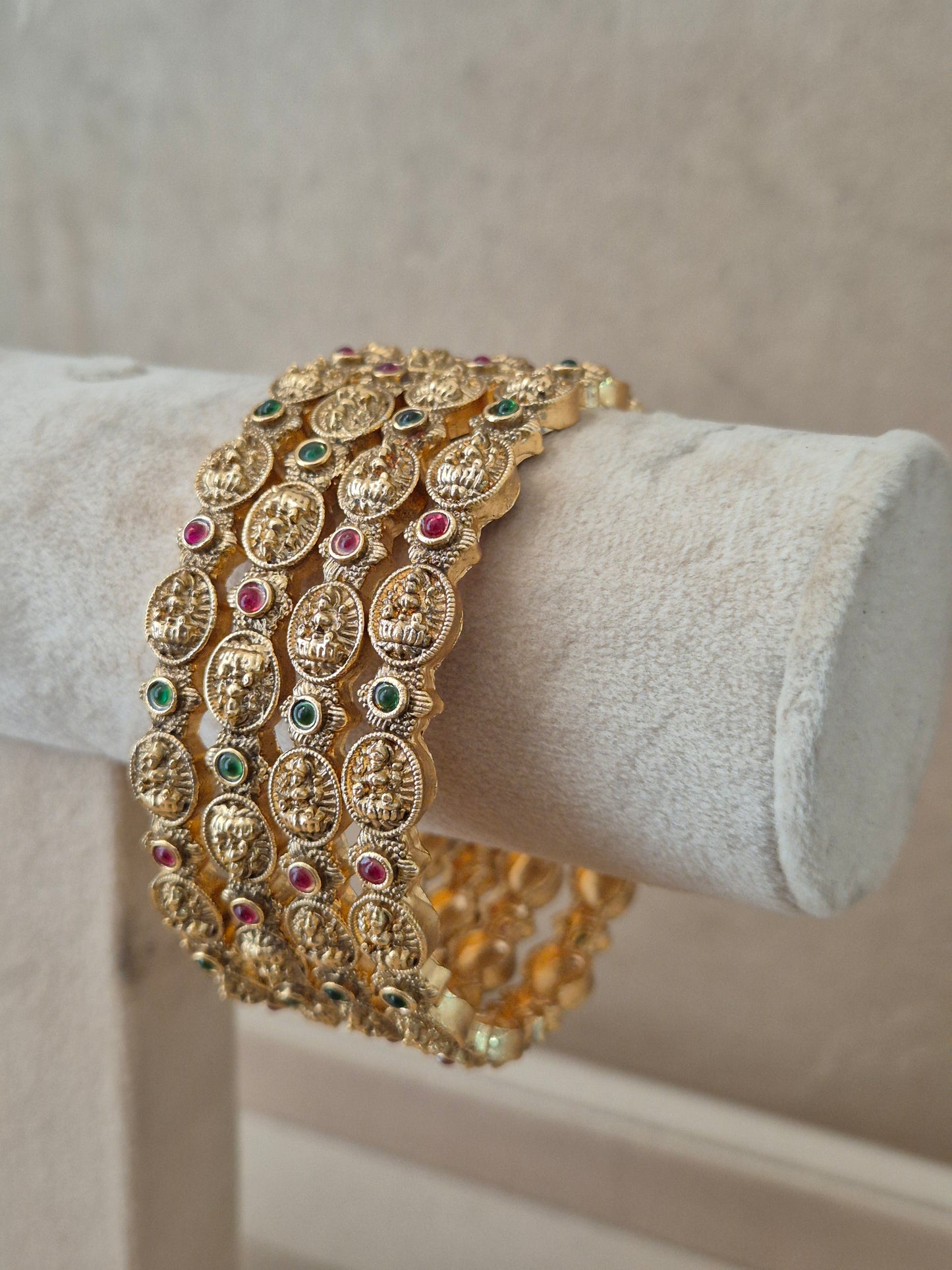 Antique style golden statement bangles with ethnic gemstone details exhibited on a neutral luxury jewelry display next to small white flowers by naitri.in 