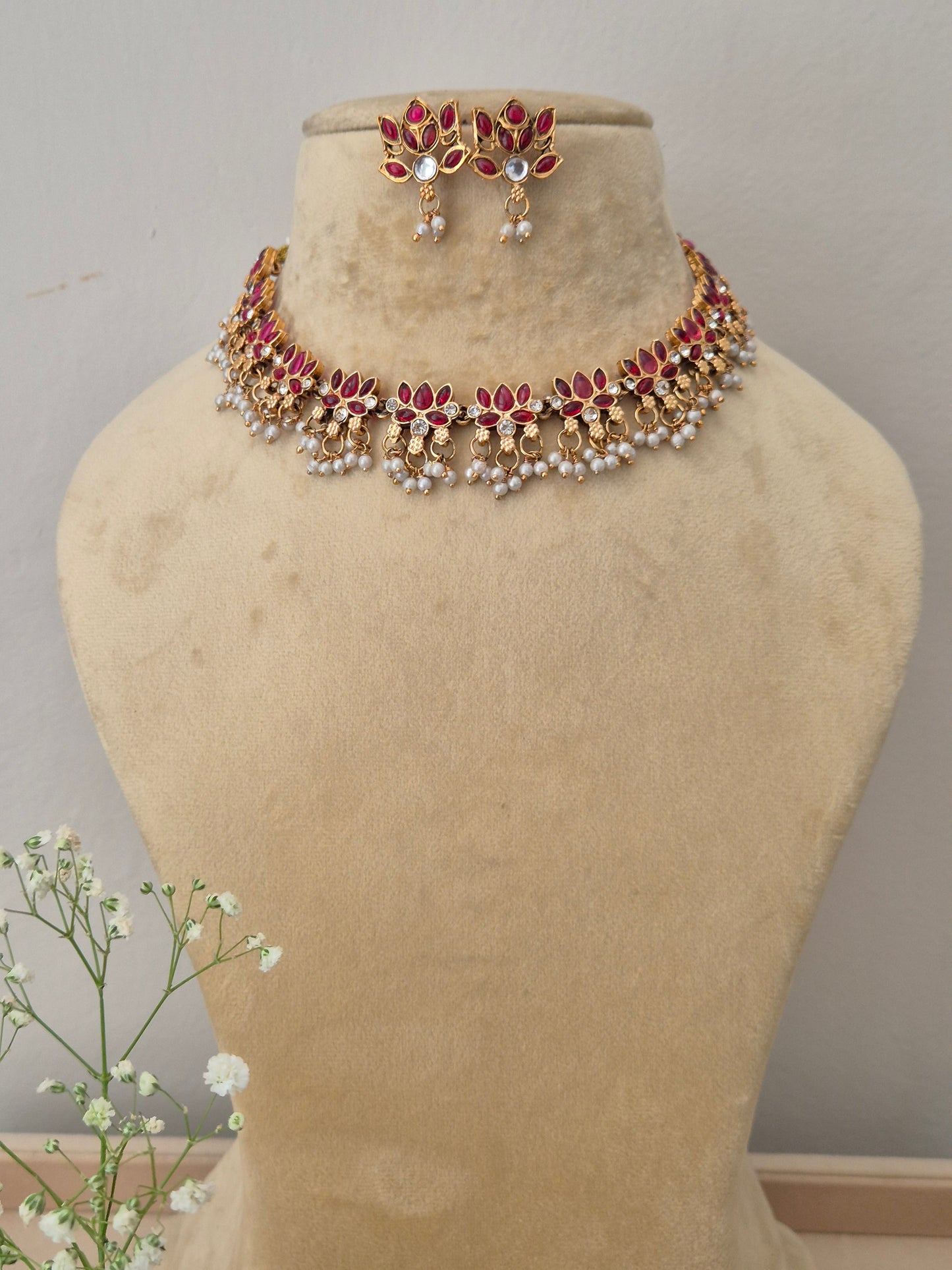 Hemangini Necklace Set by Naitri: A gold-plated ethnic choker necklace featuring a row of leaf-shaped red stones with hanging pearl clusters with matching stud earrings by naitri.in