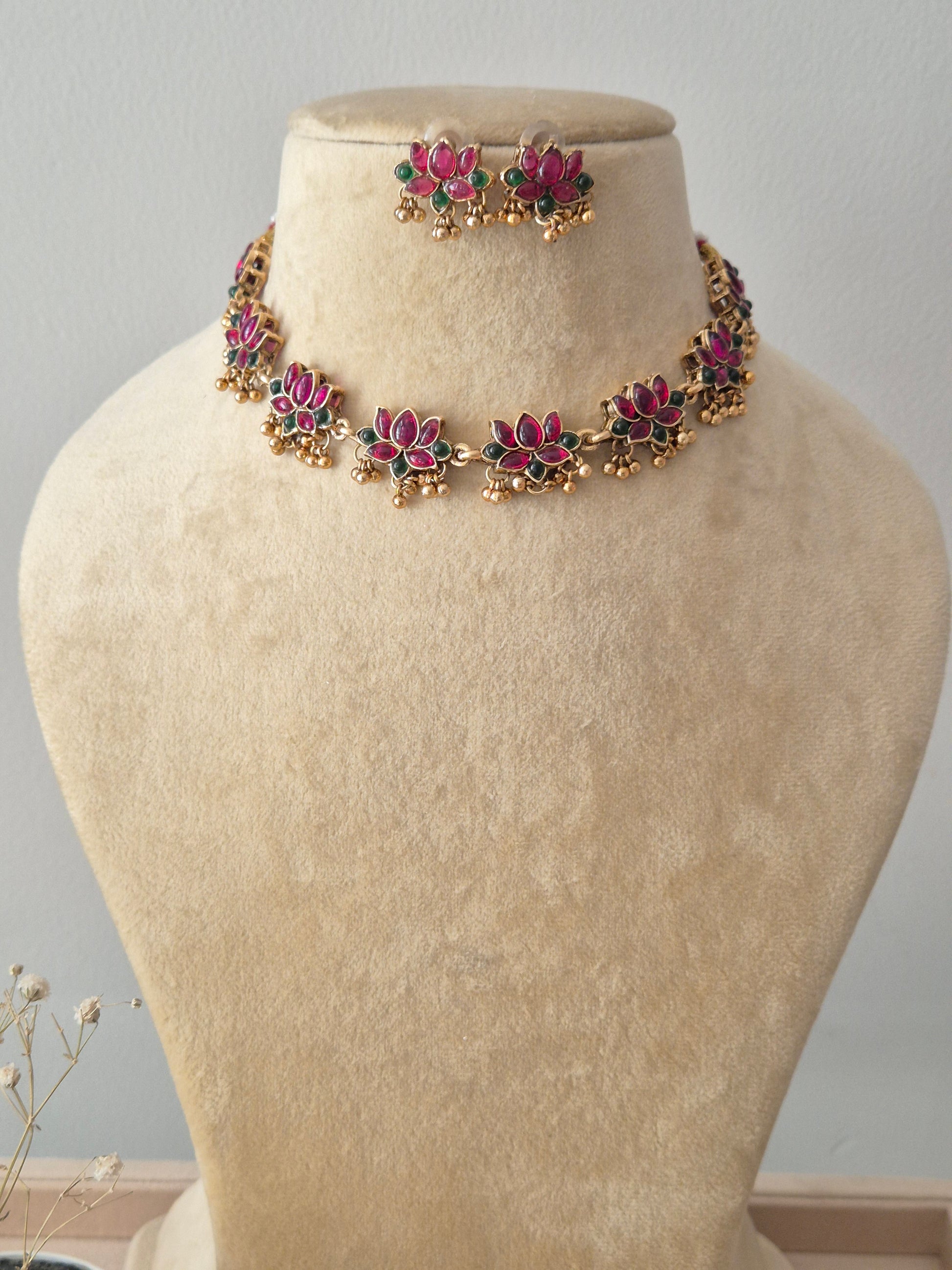 Necklace Set featuring a gold-toned choker with multiple lotus-inspired floral motifs, red and green gemstone accents, and matching small floral stud earrings by nairi.in