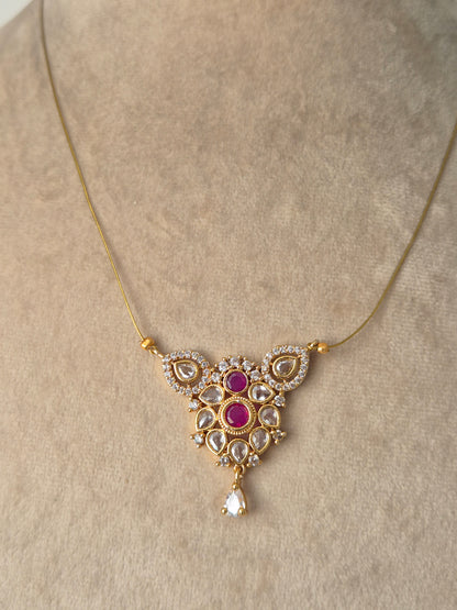 A delicate gold necklace  featuring an ornate central pendant with pink gemstones surrounded by small white stones in a floral and teardrop design, finished with a single dangling teardrop gem by naitri.in