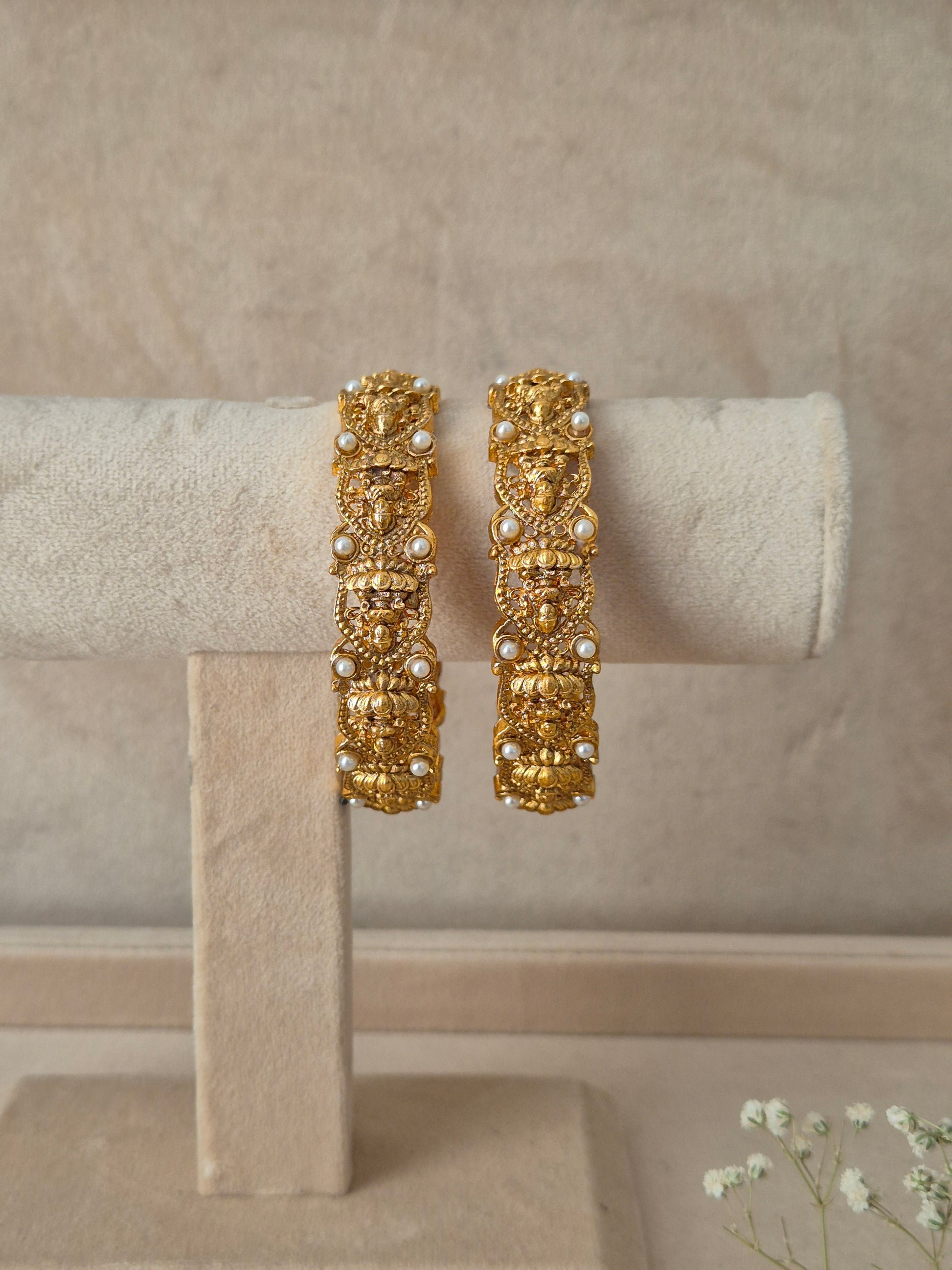 A pair of gold-plated Hitivika bangles featuring intricate traditional metalwork engraving and delicate white pearl accent beads by naitri.in
