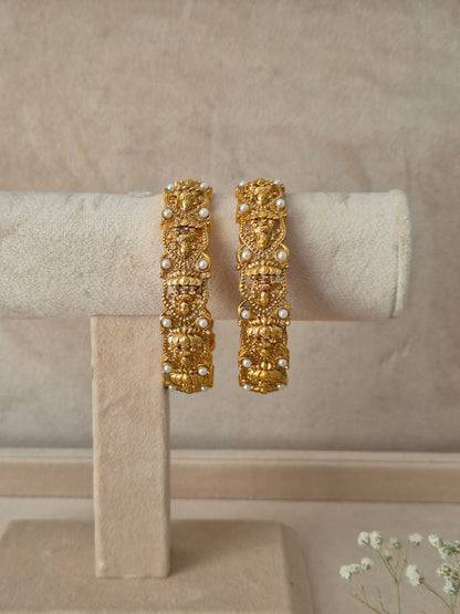 A pair of gold-plated Hitivika bangles featuring intricate traditional metalwork engraving and delicate white pearl accent beads by naitri.in